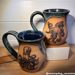 Op de afbeelding: Twee keramische mokken met een donkerblauwe glazuur en een lichtbruin interieur. Elke mok heeft een zwart-witte illustratie van een octopus.