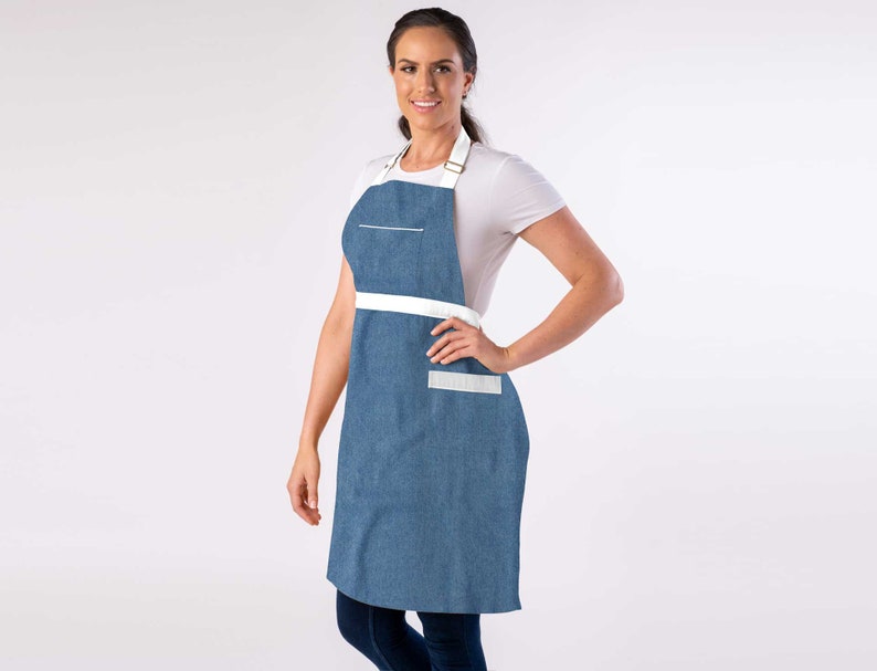 May include: A blue denim apron with white straps and a white pocket. The apron has a white stripe across the waist.