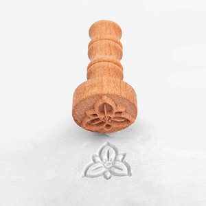 May include: A wooden stamp with a floral design. The stamp is used to create impressions in clay or dough.