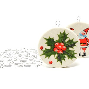 May include: Two round, white, ceramic Christmas ornaments with a red and green holly design and a Santa Claus design. The ornaments have silver wire hangers. A pile of silver wire hangers is in the foreground.