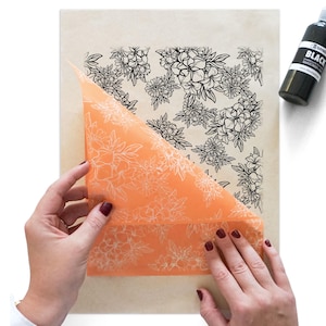 May include: An orange sheet with a floral design is being peeled back to reveal a floral pattern underneath. The floral pattern is black and white. A black bottle with white text is in the upper right corner.