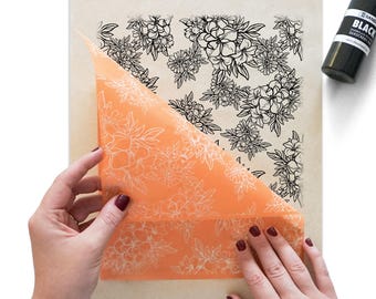 May include: An orange sheet with a floral design is being peeled back to reveal a floral pattern underneath. The floral pattern is black and white. A black bottle with white text is in the upper right corner.
