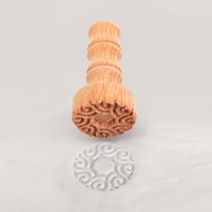 May include: A wooden stamp with a decorative design. The stamp is used to create an imprint in clay or dough.