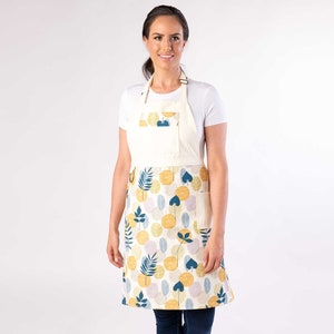 K&ouml;nnte beinhalten: Eine wei&szlig;e Sch&uuml;rze mit einem gelben, blauen und rosa Blumenmuster. Die Sch&uuml;rze hat eine gro&szlig;e Tasche auf der Vorderseite und verstellbare Tr&auml;ger.