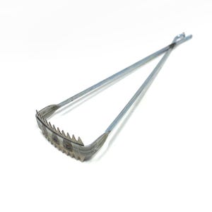 May include: A silver metal garden tool with a toothed edge and long handles. The tool has a curved, toothed section and two long, straight handles that meet at the top. The teeth are evenly spaced along the curved edge. The tool is designed for gardening.