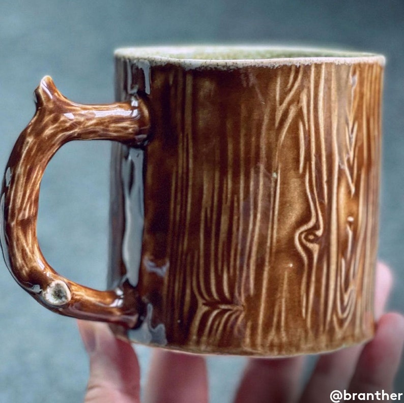 May include: A brown ceramic mug with a tree trunk design. The mug has a unique, brown, twig-shaped handle.
