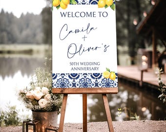 May include: Welcome to Camila + Oliver's 50th Wedding Anniversary sign with a blue and white tile pattern and lemons. The sign is on a wooden easel.