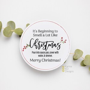 May include: A white circular Christmas-themed label with red trim and text. The text reads "It's Beginning to Smell a Lot Like Christmas" with additional instructions and a "Merry Christmas" greeting. Eucalyptus sprigs frame the label.