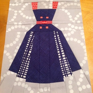 May include: A blue and white patterned fabric dress with red accents. The dress is on a gray background with white polka dots.