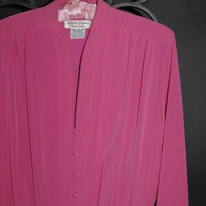 May include: A bright pink dress with long sleeves and a mandarin collar, hanging on a pink hanger. The dress features vertical pleats down the front and a row of buttons. The label reads "Adolph Schuman Lilli Ann".