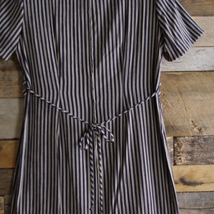 May include: A navy blue and white striped dress with short sleeves and a matching tie belt. The dress features vertical stripes and a button-up front. The tie belt cinches the waist, creating a flattering silhouette. The dress is made of a lightweight fabric.