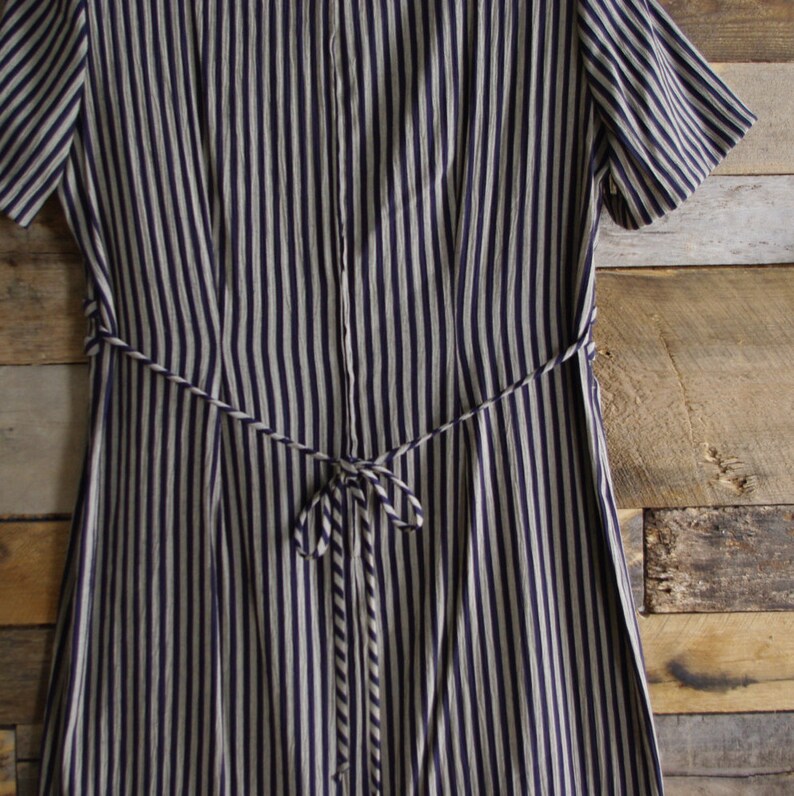 May include: A navy blue and white striped dress with short sleeves and a matching tie belt. The dress features vertical stripes and a button-up front. The tie belt cinches the waist, creating a flattering silhouette. The dress is made of a lightweight fabric.