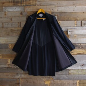 May include: A dark navy blue coat with a classic design, hanging on a wooden hanger. The coat is open, revealing a matching navy blue interior lining. The coat has a tailored fit and a collar.