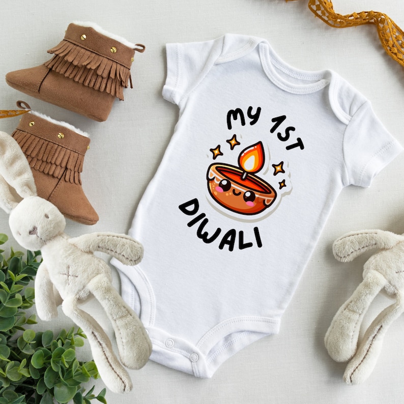 A white bodysuit with black text and a brown candle cartoon next to baby toys and shoes