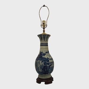 May include: A blue and white ceramic table lamp with a landscape design. The lamp has a brass neck and a dark brown wooden base. The lamp is approximately 24 inches tall.