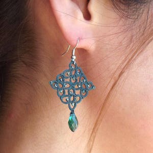 May include: A pair of dark green dangle earrings with a delicate, intricate design. The earrings feature a small, teardrop-shaped green crystal at the bottom.