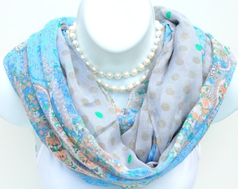 May include: A light blue and gray infinity scarf with a floral and polka dot pattern. The scarf is draped around a white mannequin head, with a double strand of pearls around the neck. The scarf has a paisley design.