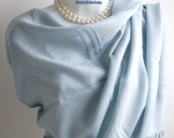 Puede incluir: Un chal azul claro drapeado sobre un maniquí, con un collar de perlas. El chal tiene un patrón sutil y flecos en el borde. La tela parece suave y fluida, creando un aspecto delicado y elegante.