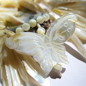 May include: A white mother of pearl butterfly pendant with a beaded necklace. The butterfly is carved with intricate details and has a pearlescent sheen.