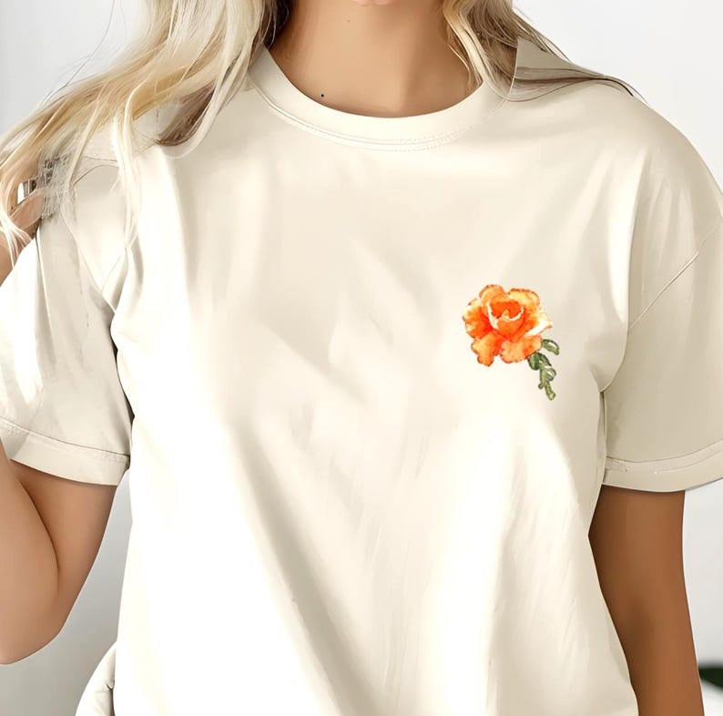 Op de afbeelding: Een wit T-shirt met een kleine, geborduurde oranje roos op de linker borst.