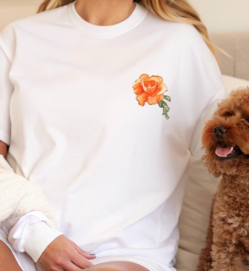 Op de afbeelding: Wit T-shirt met een oranje geborduurde roos op de linker borst.