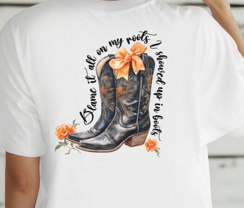 May include: White t-shirt with a graphic of brown cowboy boots with orange flowers and the text "Blame it all on my roots I showed up in boots."