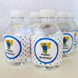 Op de afbeelding: Verschillende doorzichtige plastic waterflessen met witte doppen. Elke fles heeft een etiket met een stripfiguur en de tekst "Happy Birthday!" in een blauwe cirkel met een stippelachtergrond. De flessen zijn gevuld met water.