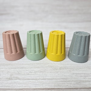 May include: Four small cups made of a textured material. The cups are in shades of pink, green, yellow, and gray.