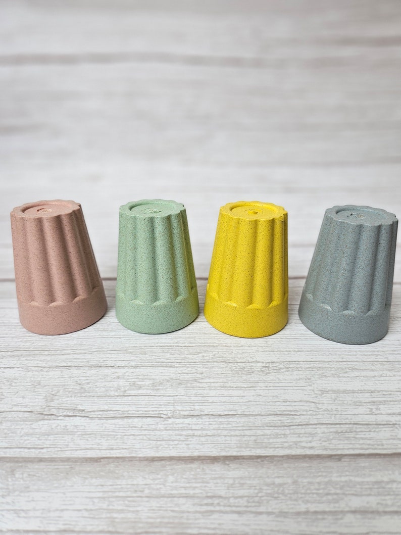 May include: Four small cups made of a textured material. The cups are in shades of pink, green, yellow, and gray.