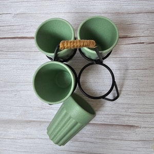 May include: Set of four green bamboo cups with a black metal stand and a woven rope handle. The cups are arranged in a circle and the stand has a circular base.