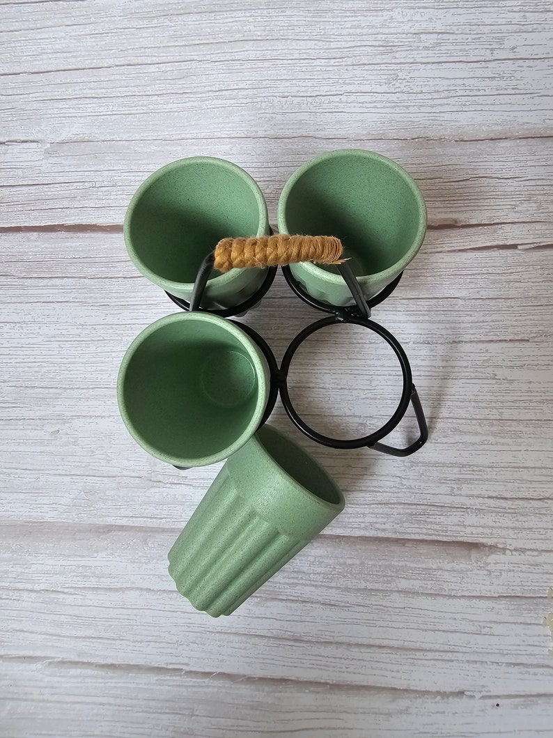 May include: Set of four green bamboo cups with a black metal stand and a woven rope handle. The cups are arranged in a circle and the stand has a circular base.