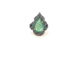 May include: A ring featuring a central pear-shaped green gemstone set in a dark metal frame. The surrounding scalloped border is encrusted with numerous small, clear pavé-set stones, creating a detailed and textured appearance around the centre.