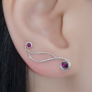 May include: A pair of silver ear cuffs with a curved design and two small pink gemstones.