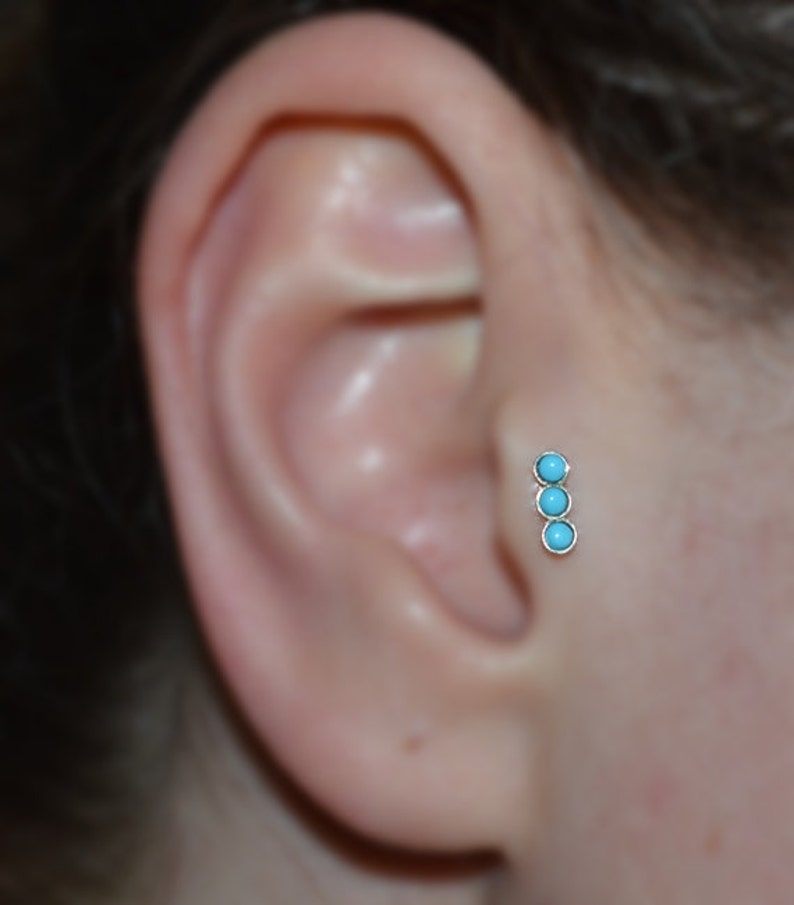 May include: A close-up of a person's ear with a silver ear piercing featuring three turquoise stones.