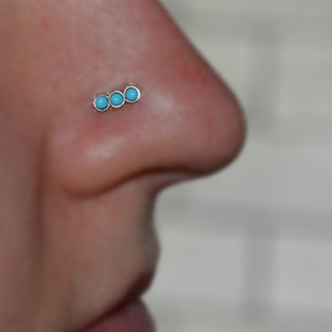 May include: A close-up of a nose piercing with three turquoise stones.