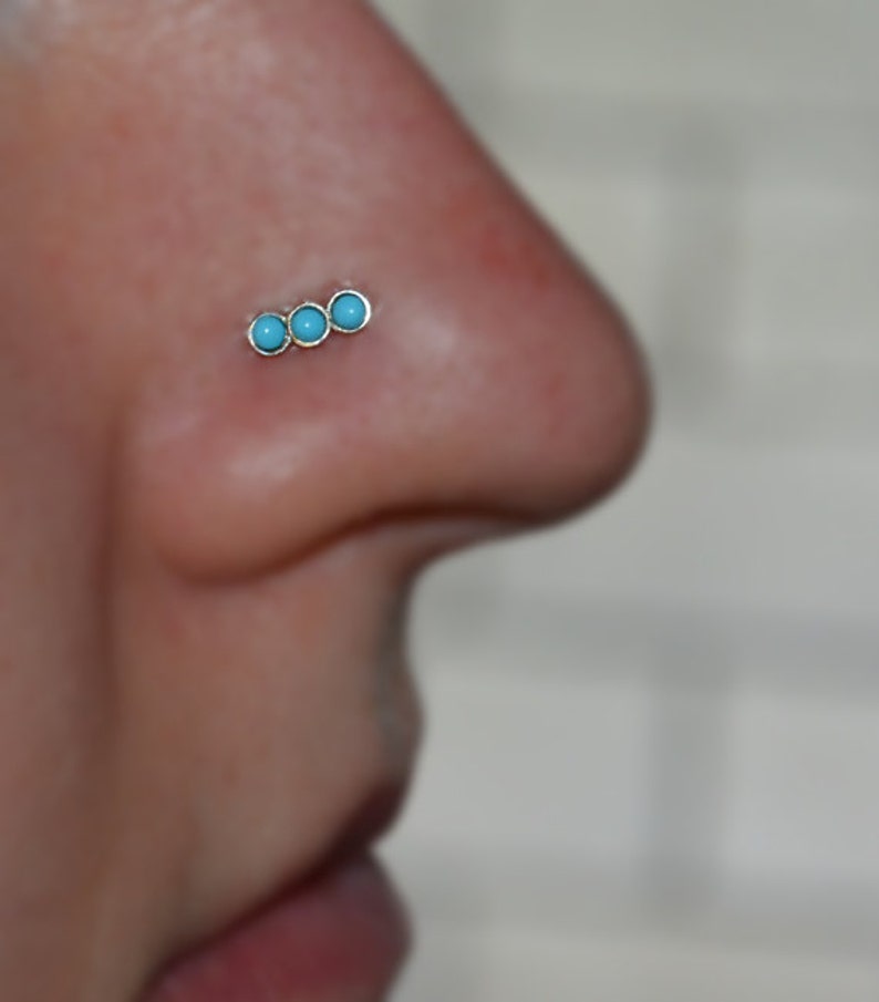 May include: A close-up of a nose piercing with three turquoise stones.