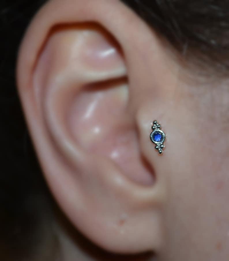 Op de afbeelding: Een close-up van een oor met een kleine zilveren oorbel met een blauwe edelsteen.