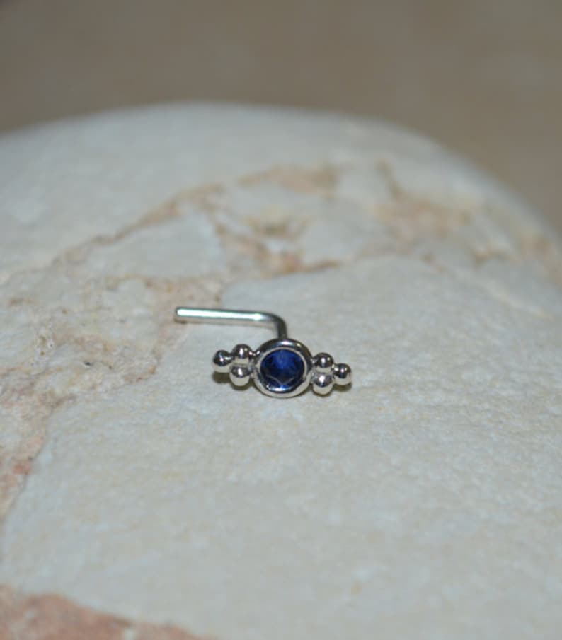 Op de afbeelding: Een zilveren neusring met een blauwe edelsteen en kleine kralen aan beide zijden.