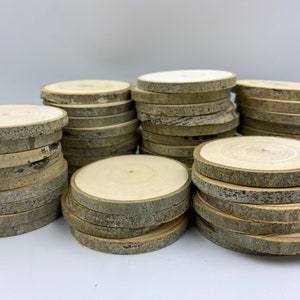 May include: A stack of round wood slices with bark, perfect for crafting projects. The wood slices are natural in color and have a rustic look.