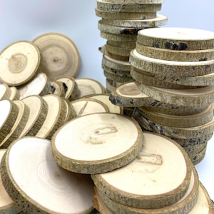 May include: A pile of natural wood slices, some stacked in a tower, with the bark still attached. The wood is light brown with a natural grain pattern.