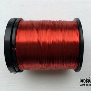 May include: A spool of red metallic thread wound around a black plastic bobbin. The thread is shiny and has a metallic sheen.