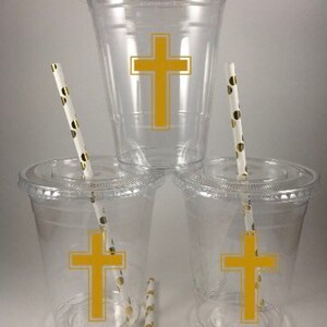 May include: Three clear plastic cups with gold cross designs and gold-dotted straws. The cups are perfect for a baptism or communion party.