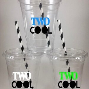 May include: Three clear plastic cups with black and white striped straws. Each cup has a sticker that says "TWO COOL" with a pair of sunglasses. The sunglasses are blue, green, and white.