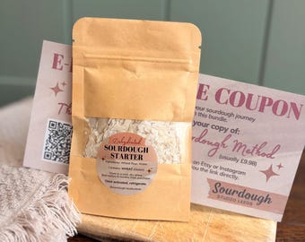 May include: A tan paper pouch containing dehydrated sourdough starter with a circular label reading Dehydrated SOURDOUGH STARTER, ingredients, and storage instructions. Behind the pouch is a coupon card with text and a QR code.