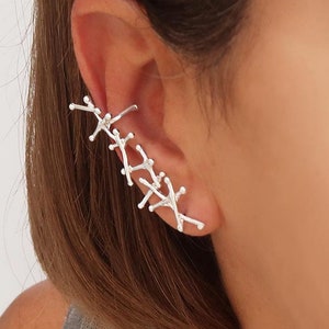 May include: Silver ear cuff with a delicate, branching design. The cuff is worn on the upper part of the ear, and it has a minimalist, modern aesthetic.