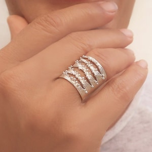 May include: A silver ring with a textured design. The ring is made of multiple bands that are stacked on top of each other. The bands are decorated with small beads.