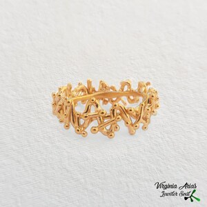 May include: A gold ring with a unique, intricate design featuring a series of interconnected lines and small circles.