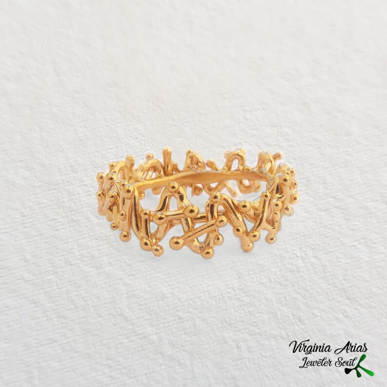 May include: A gold ring with a unique, intricate design featuring a series of interconnected lines and small circles.