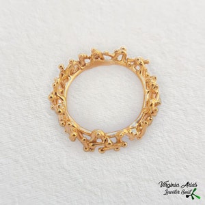 May include: A gold ring with a unique design featuring a series of interconnected figures. The ring is made of a smooth, polished metal and has a delicate, intricate design.