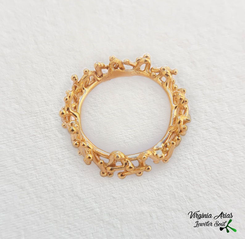 May include: A gold ring with a unique design featuring a series of interconnected figures. The ring is made of a smooth, polished metal and has a delicate, intricate design.